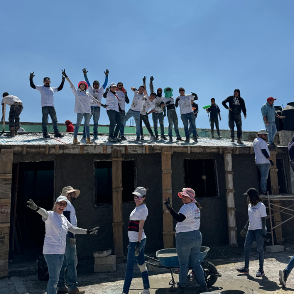 People stand on the roof of a school they are building in Mexico City. The people on the roof are waving their hands and there are people on the ground below them.